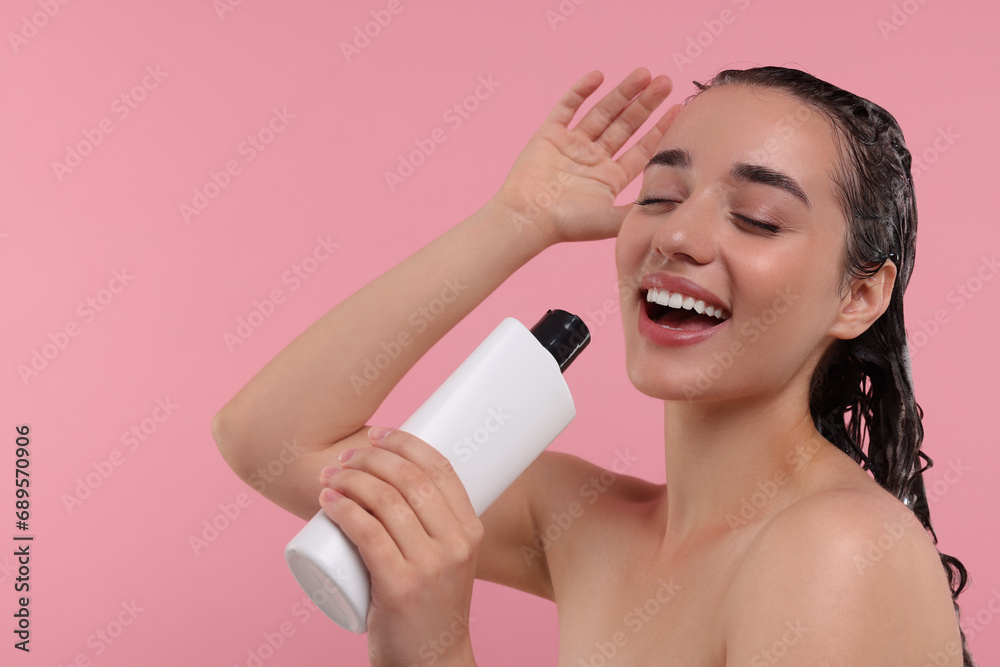Washing hair. Portrait of beautiful happy woman with bottle singing on pink background. Space for text Washing hair. Portrait of beautiful happy woman with bottle singing on pink background. Space for text