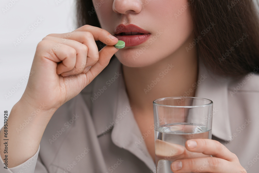Woman with glass of water taking antidepressant pill on light grey background, closeup Woman with glass of water taking antidepressant pill on light grey background, closeup