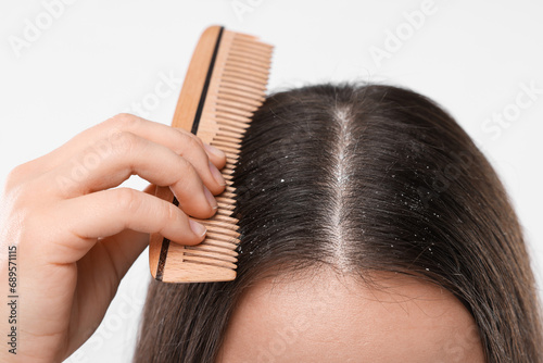 Woman with comb examining her hair and scalp on white background, closeup. Dandruff problem