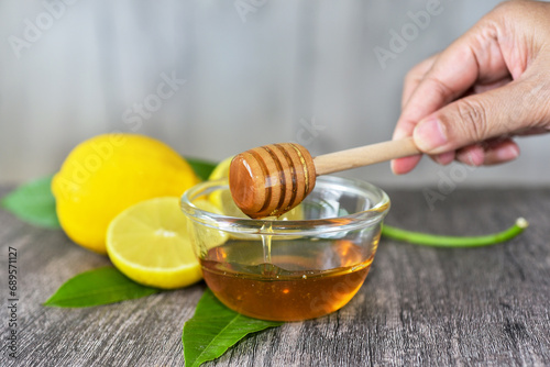 Honey bee on wooden dipper in hand with lemons background. It's natural sweetener, has antioxidant, antimicrobial, anti-inflammatory, and anticancer properties. 