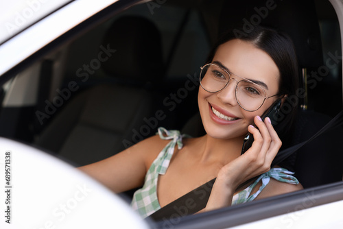 Happy young woman talking on smartphone in modern car, view from outside
