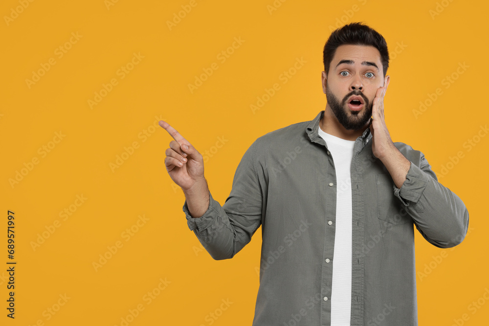 Special promotion. Surprised man pointing at something on orange background. Space for text