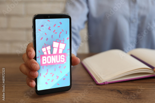 Bonus gaining. Woman showing smartphone at wooden table, closeup. Illustration of gift boxes, word and falling confetti on device screen