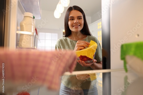Happy woman taking away beeswax food wrap, view from refrigerator photo