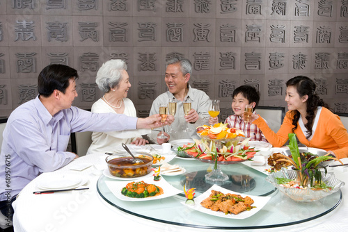 Parents and grandparents with son toasting at dinner table photo