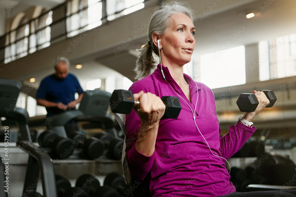 Dumbbell, fitness and senior woman at a gym for training, wellness and cardio with earphones, music or mindset. Weightlifting, bodybuilding and elderly female person at sports center for arm workout Dumbbell, fitness and senior woman at a gym for training, wellness and cardio with earphones, music or mindset. Weightlifting, bodybuilding and elderly female person at sports center for arm workout