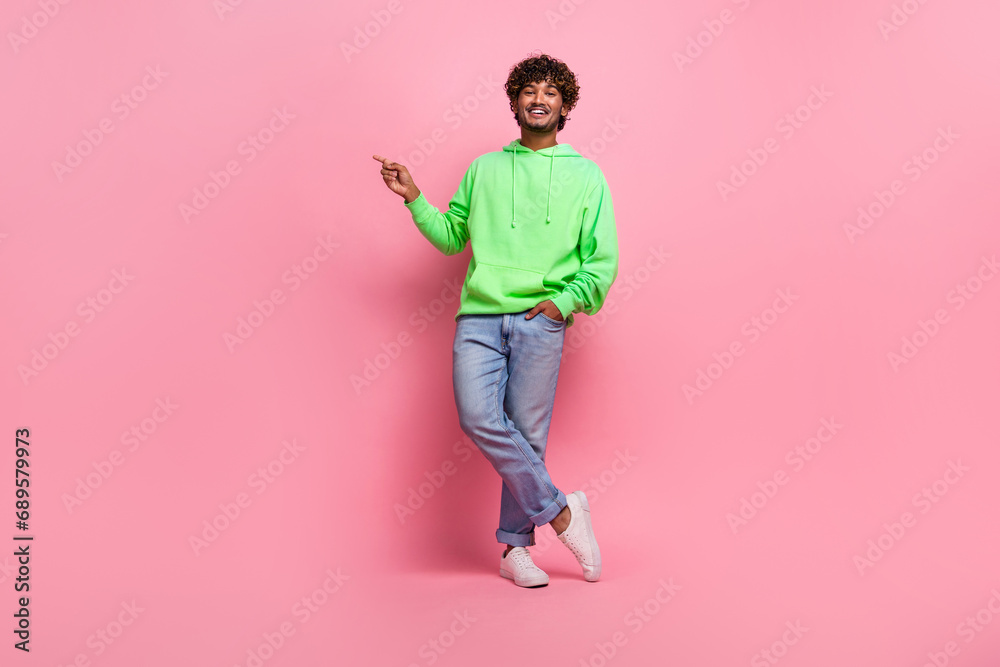 Full body size photo of young man in hoodie jeans pointing finger empty space introduce it courses club isolated on pink color background Full body size photo of young man in hoodie jeans pointing finger empty space introduce it courses club isolated on pink color background