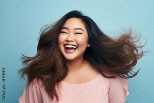 Pretty Asian plus size woman with happy smile in front of blue studio background