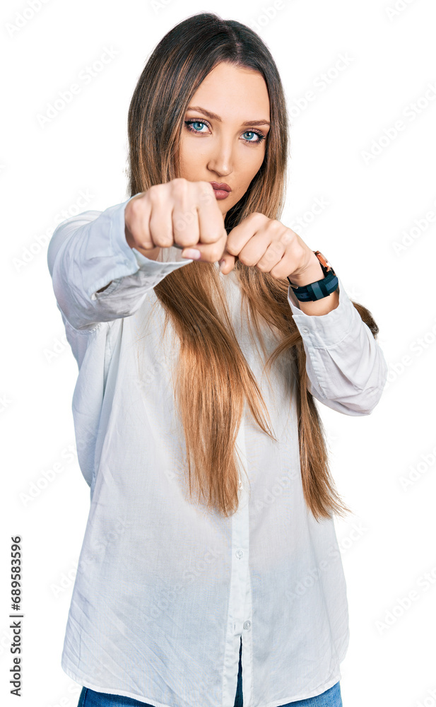 Beautiful caucasian woman wearing casual white shirt punching fist to fight, aggressive and angry attack, threat and violence Beautiful caucasian woman wearing casual white shirt punching fist to fight, aggressive and angry attack, threat and violence
