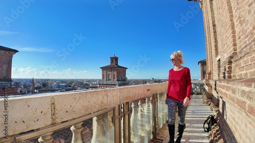 Tourist woman visiting the Ferrara castle of Italy. Surrounded by wide moat filled with water, which gives it a sense of isolation and protection. The castle has a square shape with 4 massive towers.