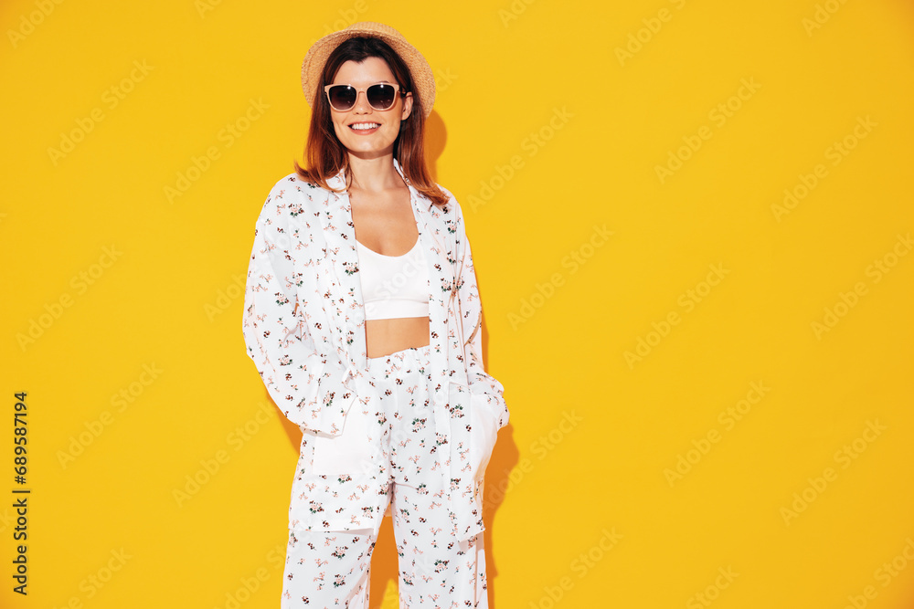 Young beautiful smiling female in trendy summer costume clothes. Carefree woman posing near yellow wall in studio. Positive model having fun indoors. Cheerful and happy. In hat and sunglasses Young beautiful smiling female in trendy summer costume clothes. Carefree woman posing near yellow wall in studio. Positive model having fun indoors. Cheerful and happy. In hat and sunglasses