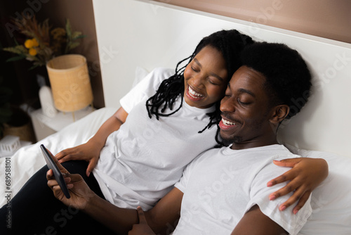 Close up shot african couple watchng funny good news lying in cozy bedroom. photo