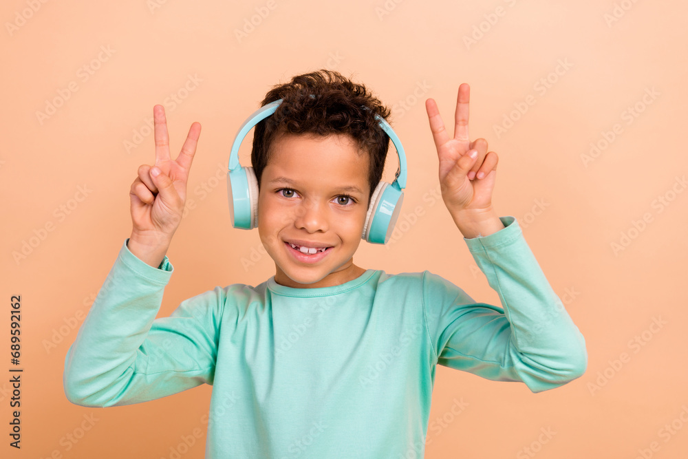 Photo of cute positive boy wear stylish cyan clothes have fun enjoy party listen mp3 plyer v-sign isolated on beige color background Photo of cute positive boy wear stylish cyan clothes have fun enjoy party listen mp3 plyer v-sign isolated on beige color background