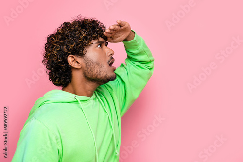 Side photo of young funny guy wearing green sweatshirt touch forehead look far away copyspace information isolated on pink color background photo