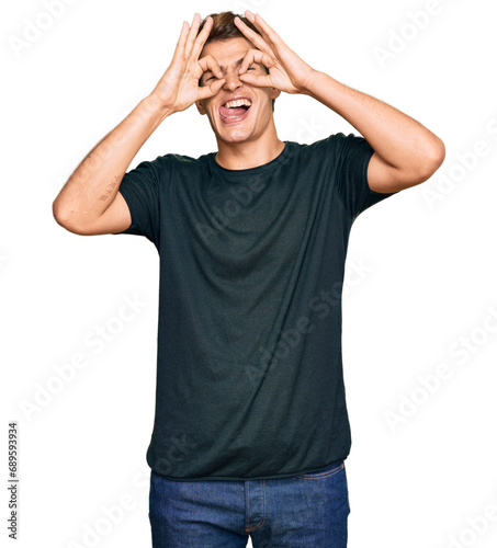 Handsome caucasian man wearing casual clothes doing ok gesture like binoculars sticking tongue out, eyes looking through fingers. crazy expression.