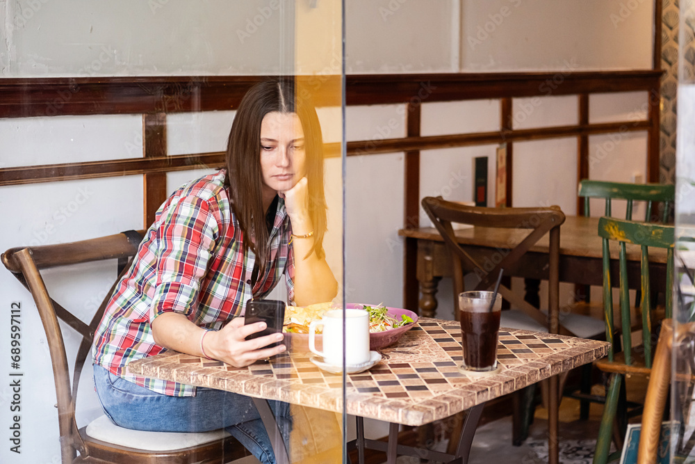Brunette woman uses smartphone while sitting in cafe in the morning.