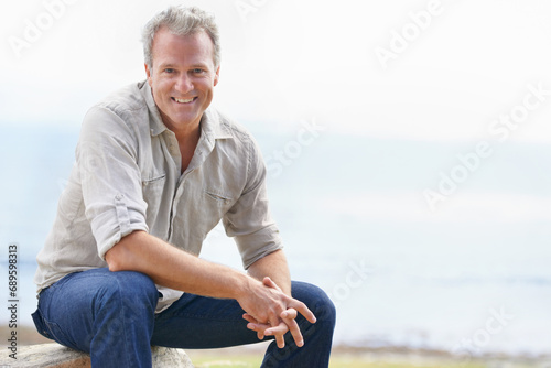 Happy, mature man and portrait on holiday at beach with freedom to relax in nature with view of ocean. Smile, outdoor and person in morning on island vacation with blue sky, sea and mockup space