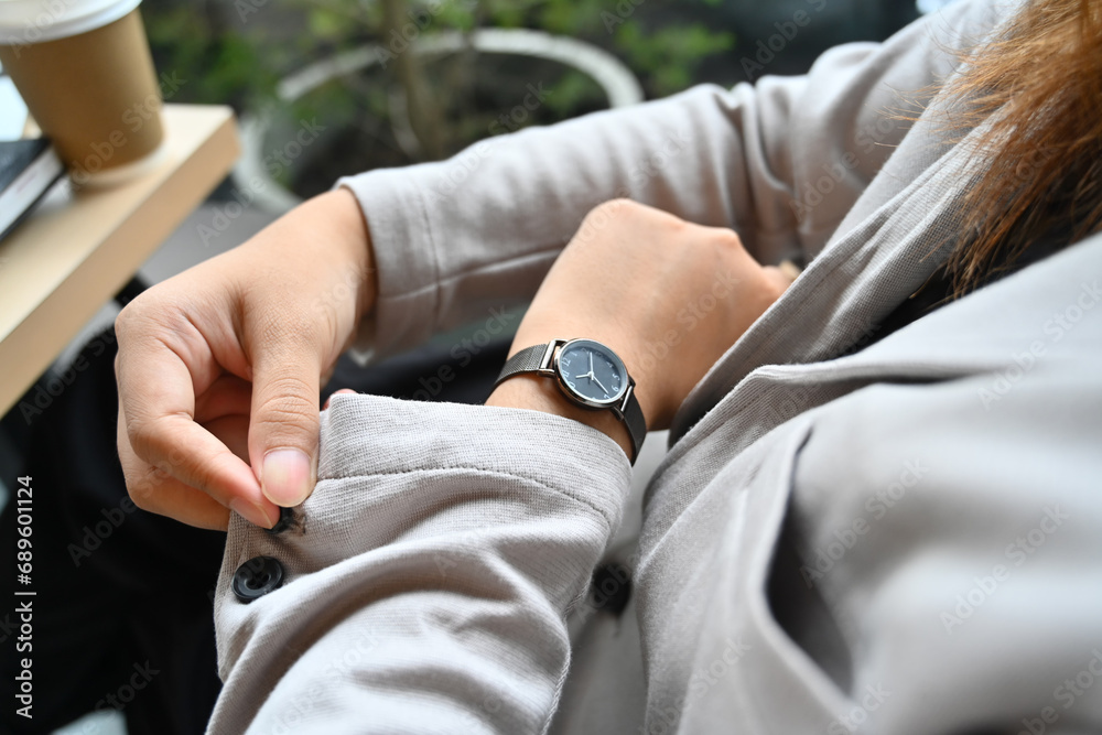 Fototapeta premium Young businesswoman buttoning up a shirt sleeve and checking time on wrist watch for appointment