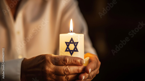 Woman holds a burning candle featuring the Star of David. Concept for International Holocaust Remembrance Day. Memory day observed on January 27 to commemorate the Holocaust. Banner, copy space photo