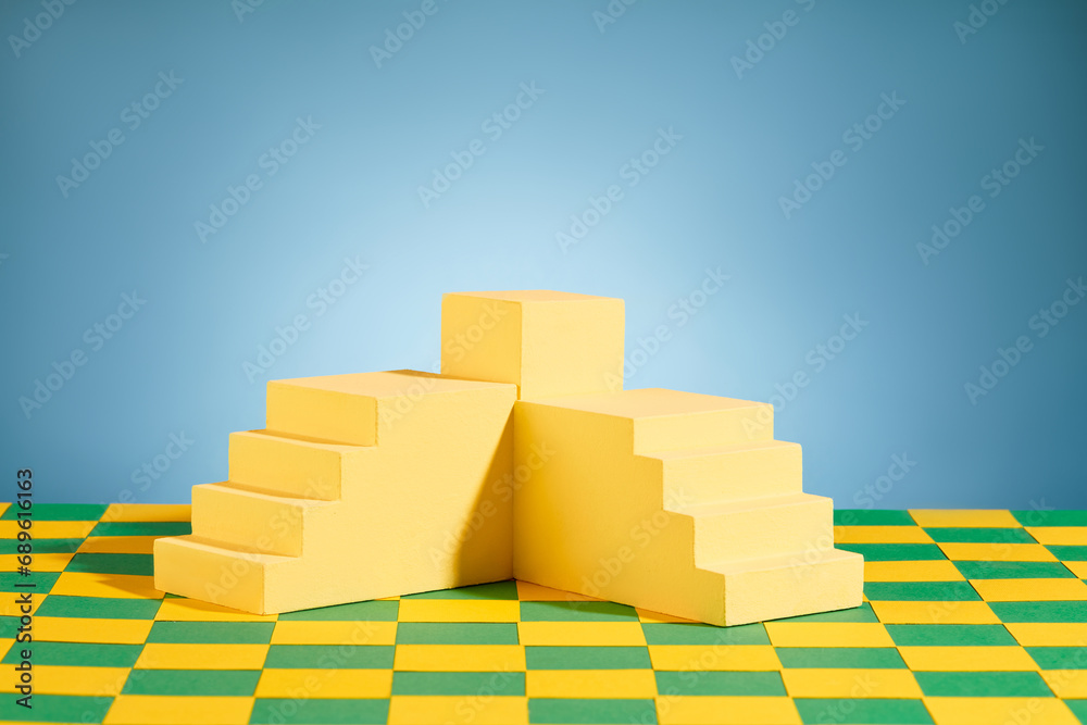 Two staircases and a rectangle podium on green and yellow checked surface with blue background. Pedestal or platform for beauty products presentation Two staircases and a rectangle podium on green and yellow checked surface with blue background. Pedestal or platform for beauty products presentation