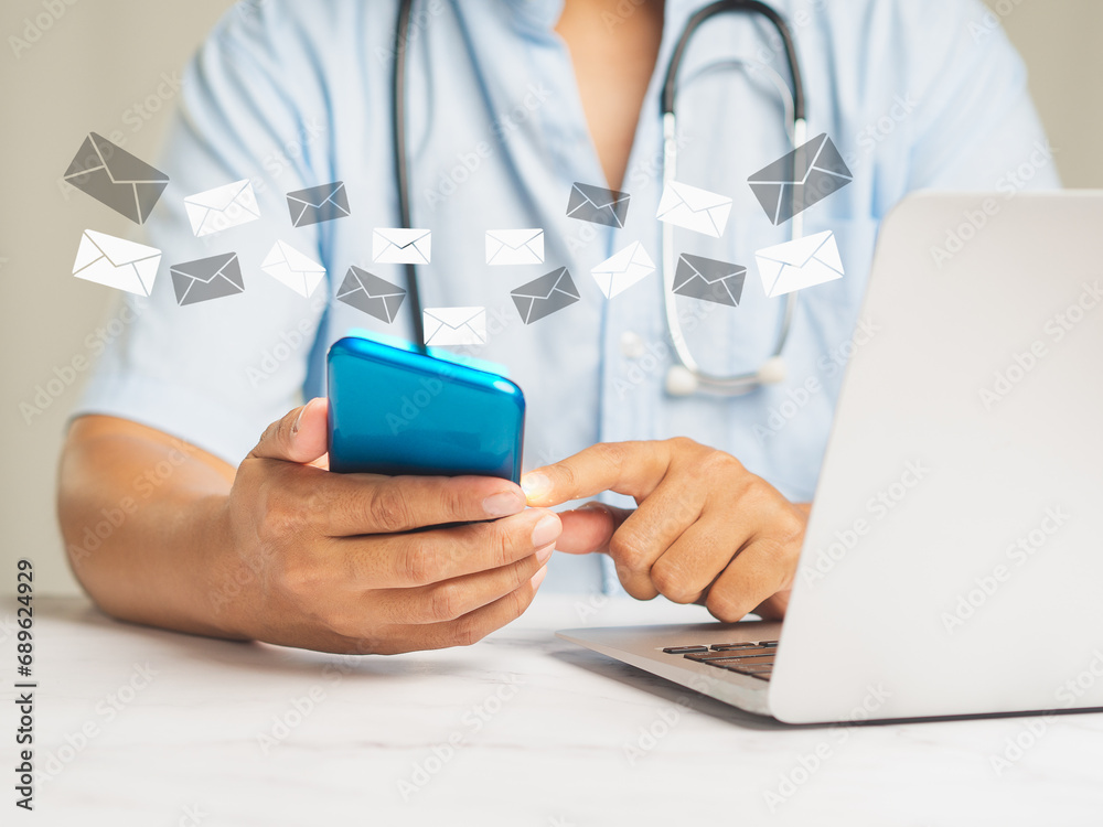 Doctor checks email on his smartphone while sitting at a desk in the hospital. Doctor checks email on his smartphone while sitting at a desk in the hospital.