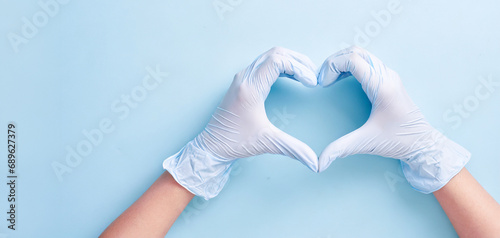 Doctor's hands in medical gloves in shape of heart on blue background with copy space. Health concept photo