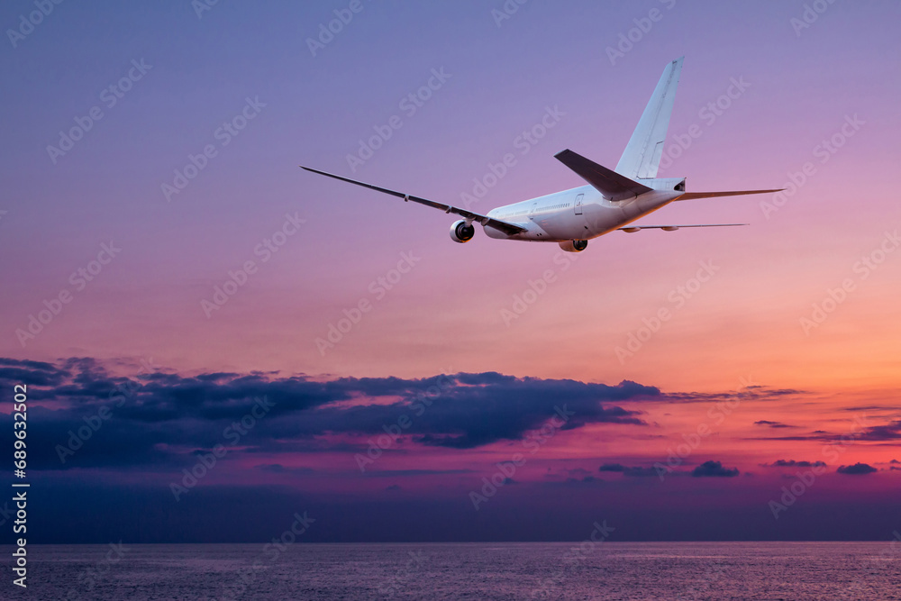 A large wide body passenger airplane takes off over the sea against the backdrop of a picturesque sunset sky