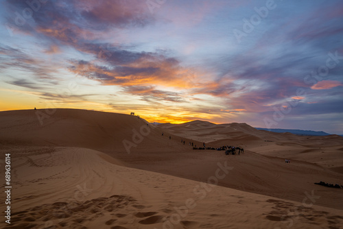 Sunset in the dunes of the Sahara desert. Camels sitting in the dunes. Sunset with some cloud and many colors