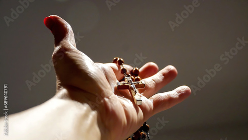 A rosary and it's cross are held in one hand, with dramatic lights on an isolated background  photo
