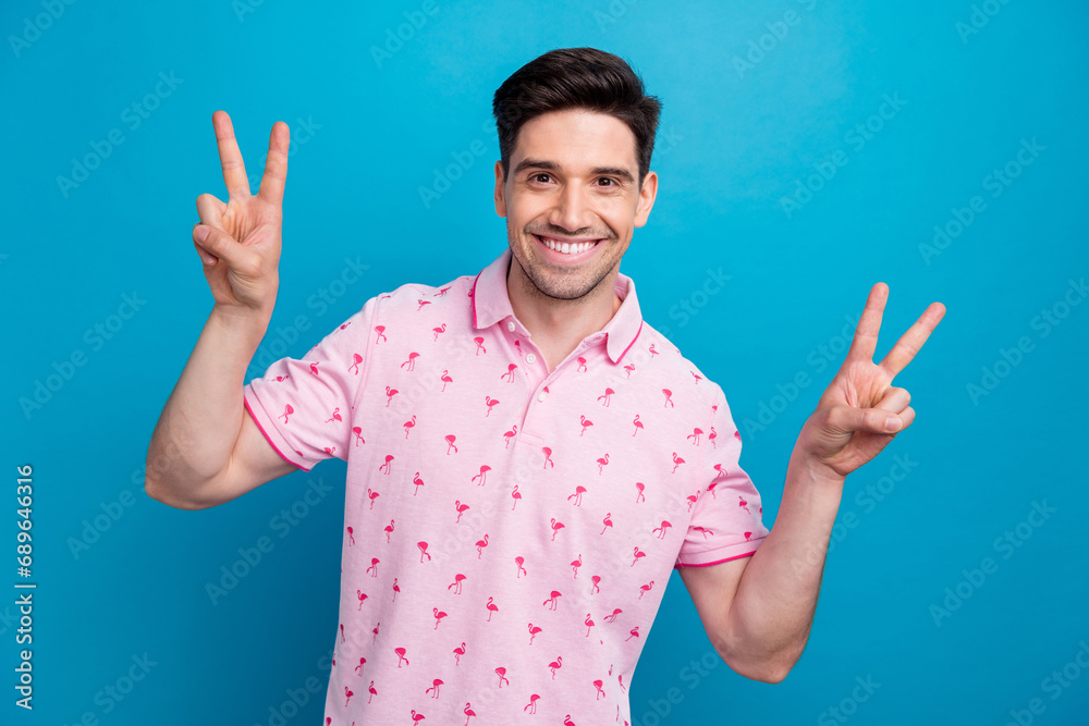 Portrait of positive satisfied young man beaming smile hands fingers demonstrate v-sign isolated on blue color background