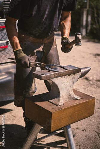 The farrier hammers the hot horseshoe on the anvil with a hammer. Horseshoeing. Sunny day.