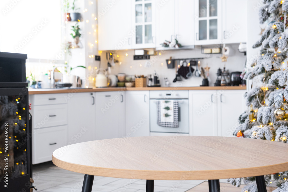 Round empty table to demonstrate the product with space for text in white kitchen, modern interior with a Christmas tree and fairy lights. New Year, Christmas mood, cozy home. 