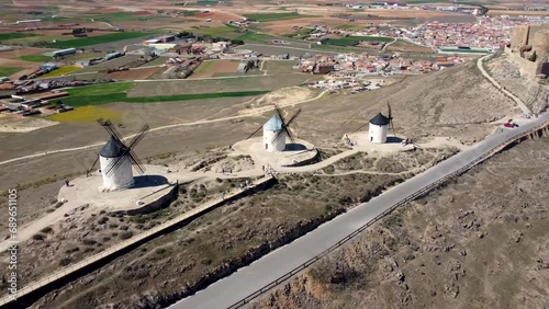 Drone panning of three old windmills in line and the Castillo de la Muela on the top of the hill with the town of Consuegra located in the province of Toledo, Spain in background