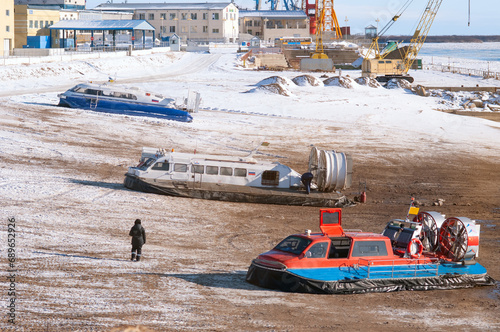 Three hovercraft on the shore of a passenger international river port on a winter sunny day. Snow and mud.