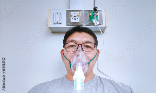 Asian adult man with asthma and respiratory diseases using nebulizer mask in inhalation therapy at hospital, front view  photo