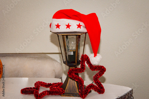 Decorated Xmas lamp with Santa hat. Christmas lantern lamp. Merry Christmas. Happy Ney Year 2024. Xmas holiday celebration. New Year eve. Santa Claus hat on lantern. December holiday light bulb photo