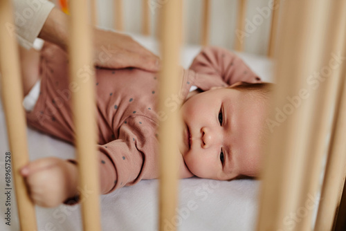 Close up shot of peaceful baby lying in cot, moms hand rubbing belly, view through crib bars