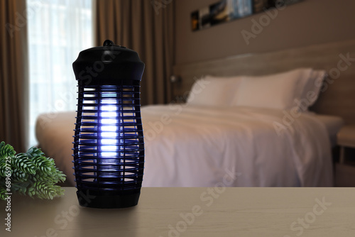 an insects mosquito electric blue light killer lamp is put on the nice wooden table in the nice bedroom to protect the mosquito during sleeping time