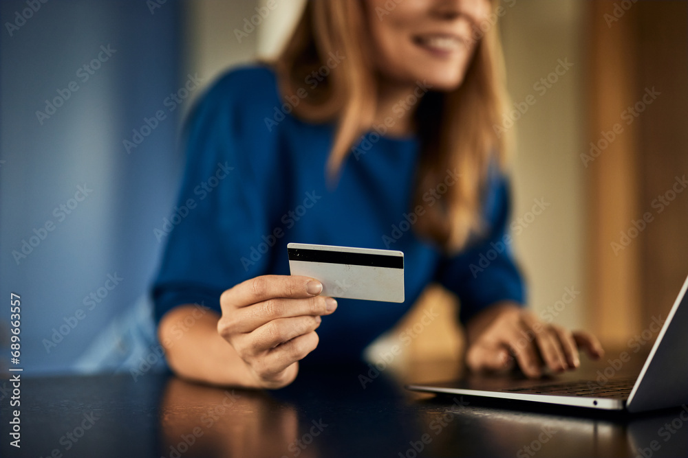 A smiling woman in the background, holding a credit card, using a laptop. A smiling woman in the background, holding a credit card, using a laptop.