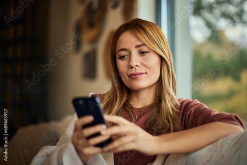 A woman using a mobile phone while sitting on the couch, smiling.