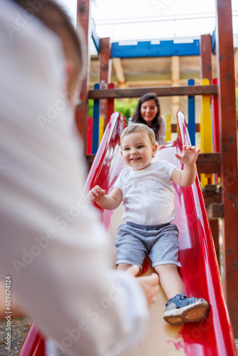 Parents having fun playing with toddler son on a slide in the park