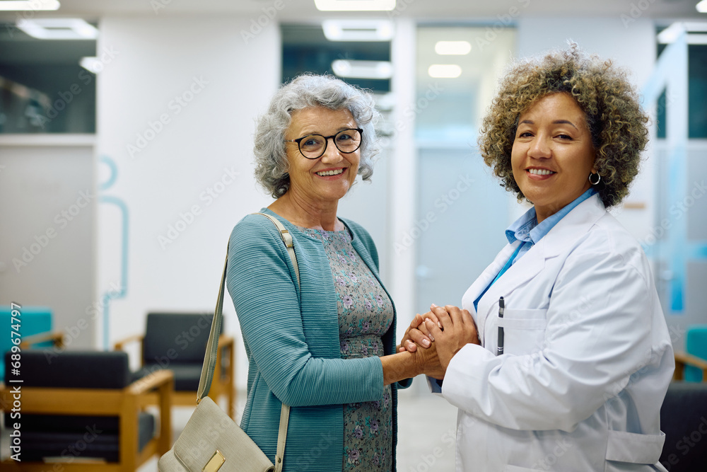 Fototapeta premium Happy senior woman holding hands with her doctor at clinic and looking at camera.