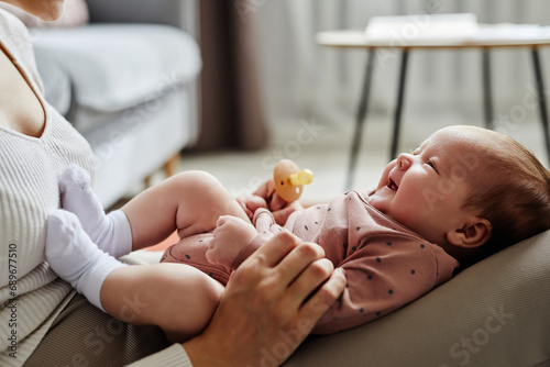 Vászonkép Side view of mother playing with laughing baby girl lying on her knees spending