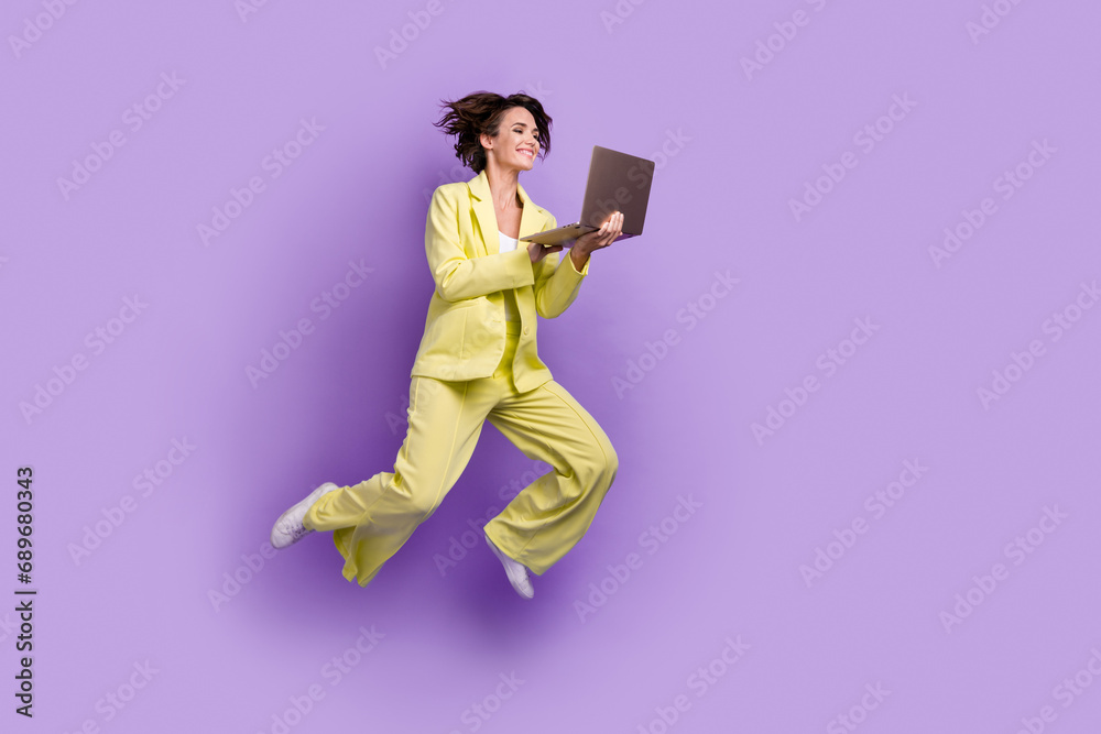 Fototapeta premium Full length photo of carefree sweet lady wear suit blazer jumping high texting modern gadget isolated violet color background
