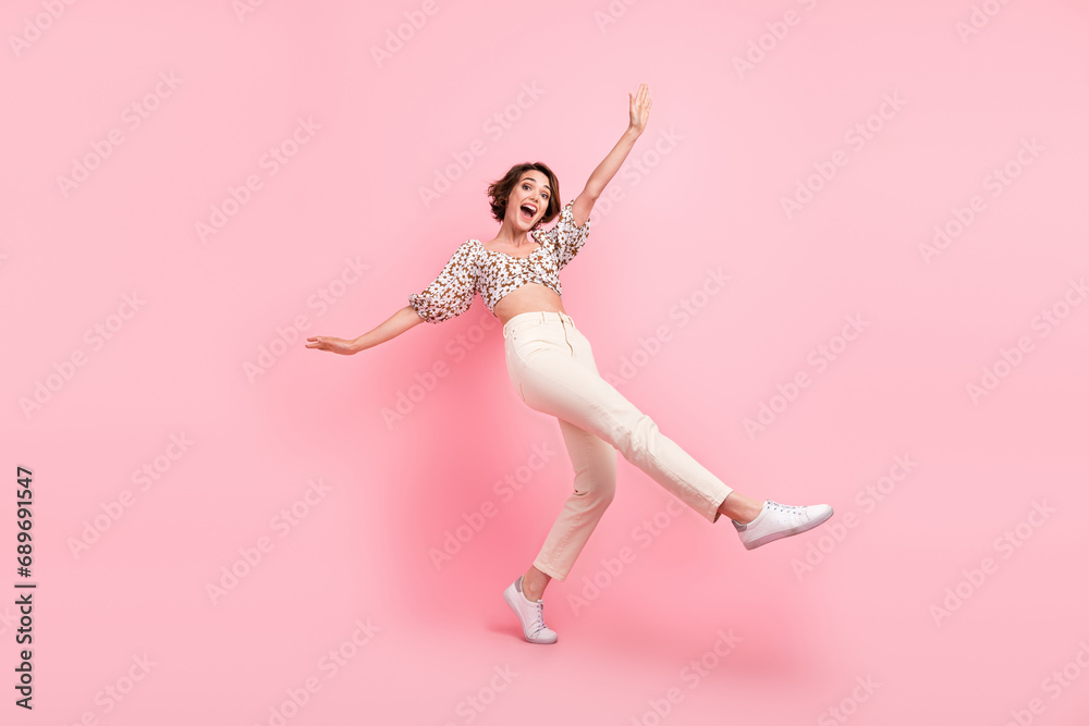 Fototapeta premium Full size photo of good mood girl dressed stylish blouse white trousers stand on tiptoe hold balance isolated on pink color background