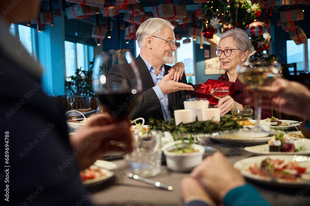 Happy man giving present to woman during festive dinner in restaurant