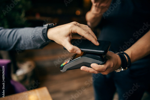 Close up of hand using app on smart phone for transaction on POS machine.