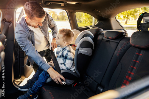 A happy dad is putting his son in his car seat. They are getting ready for travel.
