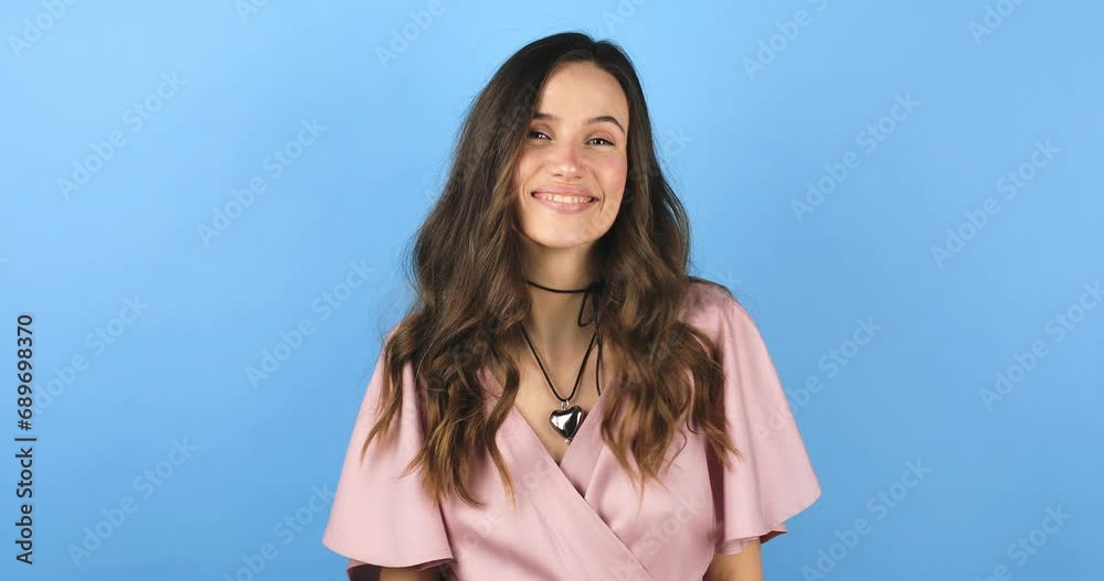 Happy friendly young woman waves palm in hello gesture welcomes someone with hospitable expression expresses positive emotions standing isolated bright blue background. Hi to all of you. Happy friendly young woman waves palm in hello gesture welcomes someone with hospitable expression expresses positive emotions standing isolated bright blue background. Hi to all of you.