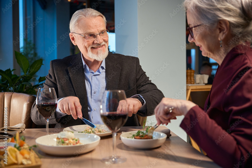 Smiling aged man and woman eating festive dinner during New Year celebration Smiling aged man and woman eating festive dinner during New Year celebration
